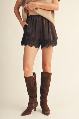 Black satin shorts with floral lace-trimmed hem and elastic waist, styled with brown suede knee-high boots.
