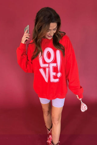 Red oversized sweatshirt with pink "LOVE!" graphic print, modeled with white biker shorts and cowboy boots.