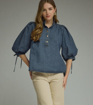 Solid dark wash denim top with dramatic puff sleeves, tie cuffs, button placket, and ruffled neckline.