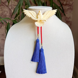 Ivory carved eagle bolo tie with red cord strings and two royal blue silk tassels on display bust.