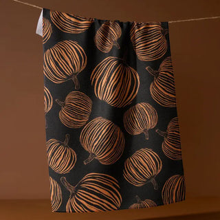 Black tea towel with repeating orange line-drawn pumpkin pattern, hanging on a string.