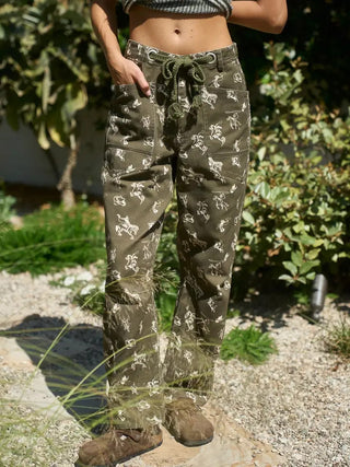 Olive green barrel pants with white western cowboy and horse print, rope drawstring waist, worn outdoors.