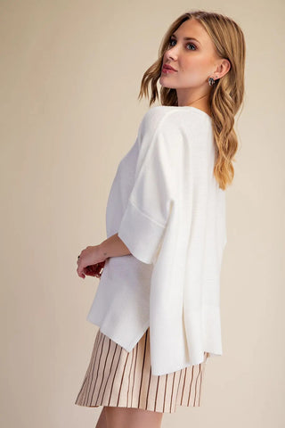 White oversized pullover sweater with three-quarter sleeves, ribbed cuffs, and side slit hem detail.