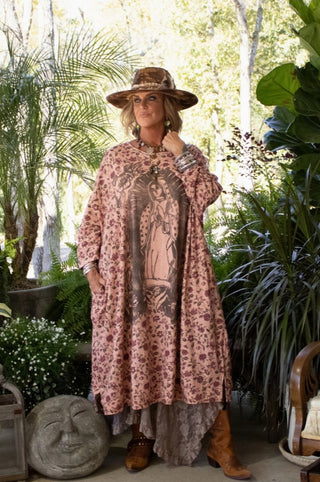Oversized pink floral tunic with Virgin Mary graphic print, worn with wide-brim hat and cowboy boots.