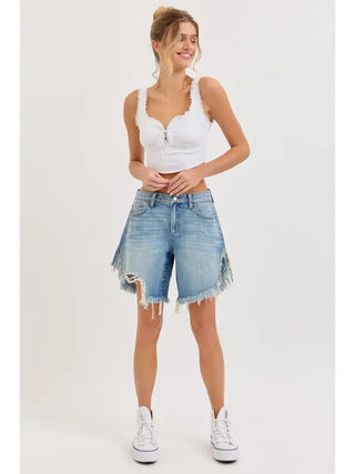 Light wash mid waist distressed denim cutoff shorts with frayed hem, worn with white crop top and sneakers.