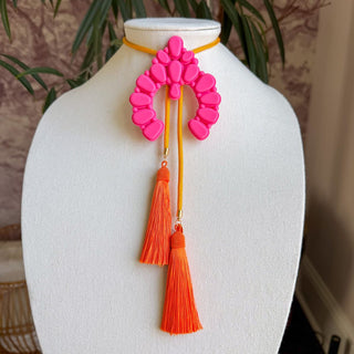 Hot pink naja-shaped bolo necklace with golden yellow cord and two orange silk tassels on white display bust.