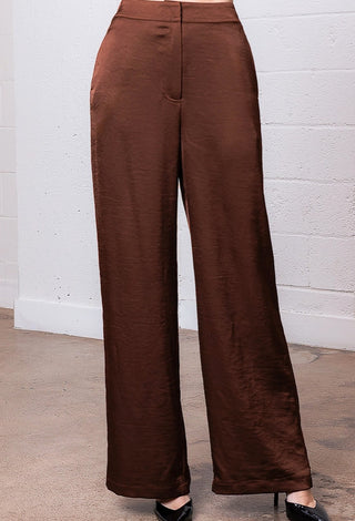 Chocolate brown satin wide-leg high-waisted pants with a smooth, lustrous finish, styled with black heels.