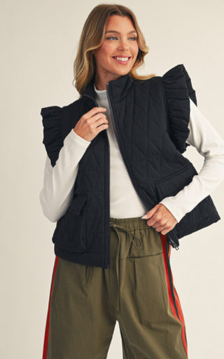 Black quilted vest with ruffle cap sleeves and front zip closure, styled over white long-sleeve top.