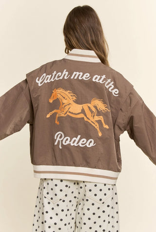 Brown bomber jacket with embroidered golden horse and "Catch Me at the Rodeo" text on back.