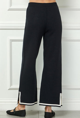Black knit wide-leg pants with white contrast stripe trim at hem and side slits.