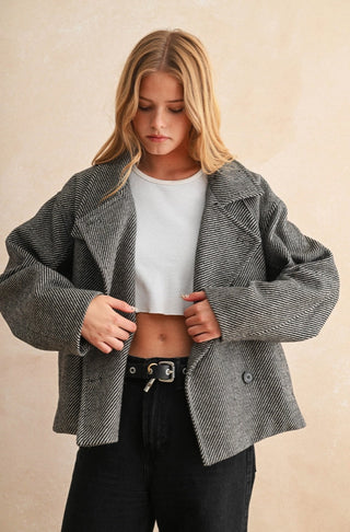 Woman wearing an oversized cropped herringbone pattern jacket in black and white over a white crop top.