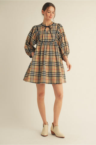 Tan plaid babydoll dress with black leather trim, 3/4 puff sleeves, tie neckline, and gathered skirt.