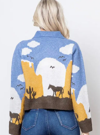 Blue knit cardigan with Western desert scene featuring horses, cacti, mesas, and clouds on back.