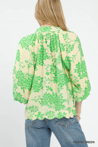 Woman wearing a light yellow blouse with bright green floral print, balloon sleeves, and scalloped hem.