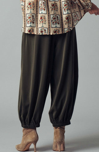 Black relaxed-fit harem pants with elastic cuffs, paired with a floral block-print top and beige heeled boots.