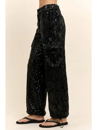 Black wide-leg sequin cargo pants with elastic cuffed ankles, worn with black flip-flops.