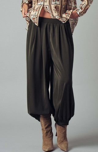 Olive green satin wide-leg pants with elastic waistband and gathered cuffed ankles, styled with tan boots.