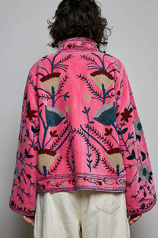 Pink velvet jacket with multicolor floral embroidery, relaxed silhouette, wide sleeves, worn with white pants.