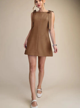 Camel brown sleeveless mini dress with shoulder bow details, A-line silhouette, center seam, paired with white Mary Jane flat