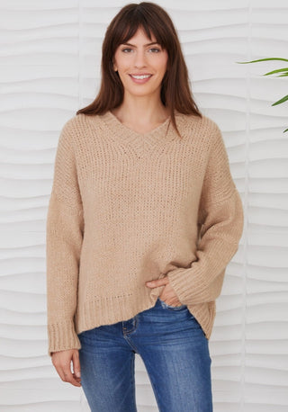 Woman wearing a camel beige fuzzy knit oversized V-neck sweater with long sleeves and blue jeans.