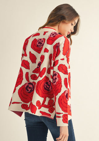 Woman wearing a cream drop-shoulder sweater with bold oversized red rose floral pattern, long sleeves.