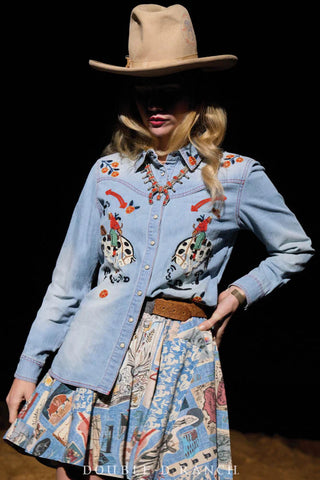 Light blue denim western snap shirt with colorful embroidered beetle and floral motifs, worn on runway model.