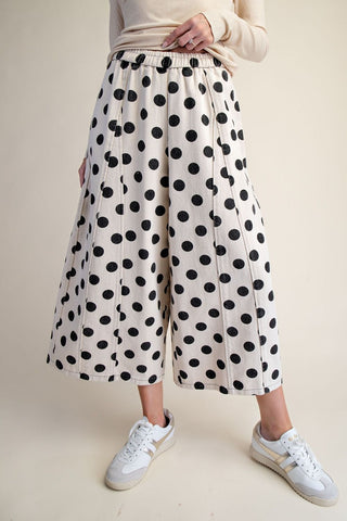 Cream wide-leg cropped pants with large black polka dots, elastic waistband, styled with white sneakers.