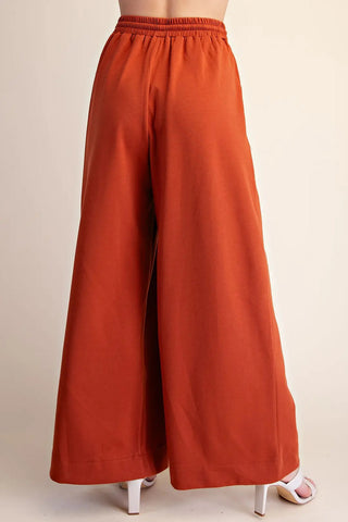 Rust orange wide-leg palazzo pants with elastic smocked waistband, shown from back view.