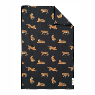 Black waffle-weave hand towel featuring an allover orange tiger print in various poses, corner folded back.