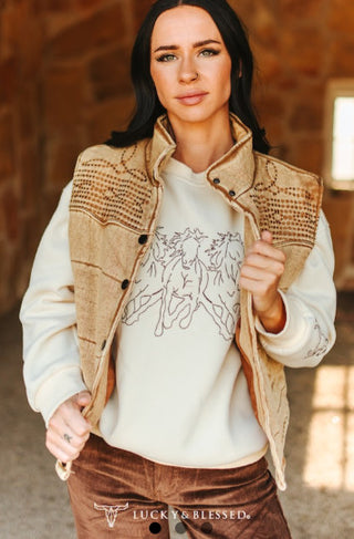 Tan studded embroidered denim puffer vest with snap buttons, worn open over cream sweatshirt.