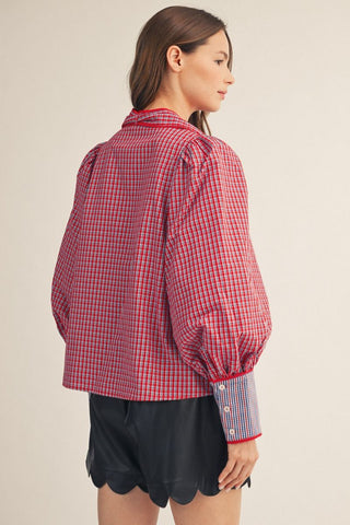 Red and navy plaid puff sleeve button-down shirt with contrast cuffs and red tie neck accent.