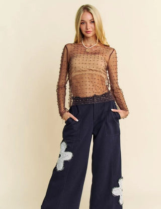 Pearl-embellished sheer brown mesh long sleeve top styled with wide-leg navy pants on blonde model.