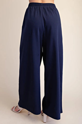 Navy blue wide-leg drawstring sweatpants with elastic waistband, shown from back view with white heels.