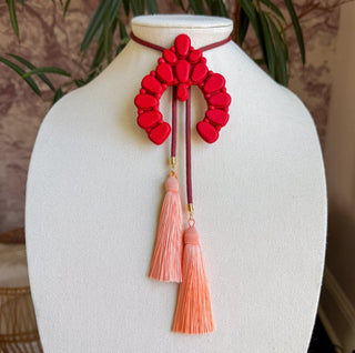 Red naja-shaped bolo necklace with maroon cord and two hanging peach tassel pendants.
