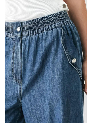 Medium wash denim pants with elastic waistband, silver button accents, and front pocket detailing.