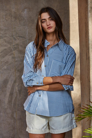 Woman wearing oversized blue and white striped woven cotton button-front shirt with collar and long sleeves.