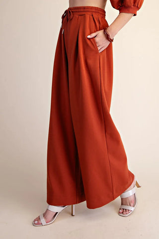 Rust orange wide-leg drawstring sweatpants with elastic waistband, pleated front, and side pockets.