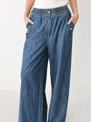 Washed blue wide-leg denim pants with elastic waistband, side pockets, and silver button details.
