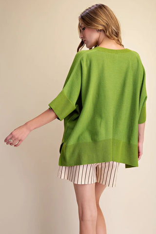 Woman wearing an oversized green knit pullover sweater with short sleeves, ribbed hem, and striped shorts.