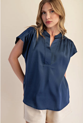 Navy blue satin blouse with V-neckline, cap sleeves, and relaxed fit, paired with white shorts.
