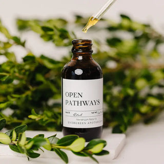 Amber glass dropper bottle labeled "Open Pathways" tincture by Evergreen Apothecary, surrounded by green botanicals.
