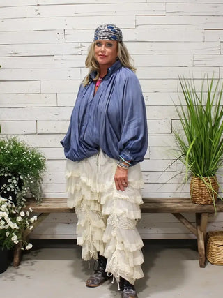 Woman wearing oversized blue satin Willow Sky Top with gathered fabric, paired with ruffled white skirt.