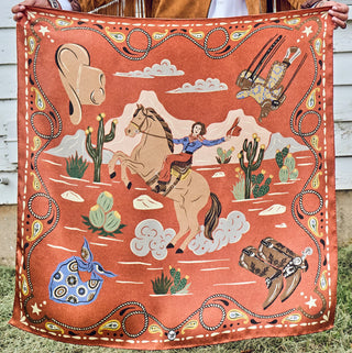 Rust-orange silk bandana featuring a cowgirl riding a horse, cacti, cowboy boots, hat, and paisley border details.