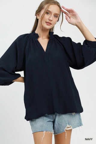 Navy balloon sleeve split neck blouse with smocked neckline, paired with distressed denim shorts.