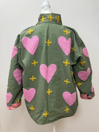 Olive green jacket with pink chenille heart patches and yellow cross embroidery, displayed on mannequin.