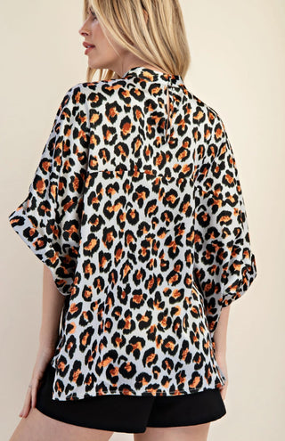 White leopard print mock neck oversized top with orange and black spots, worn with black shorts.