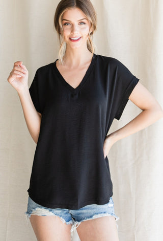 Black v-neck cap sleeve top with rolled cuffs and raw edge hem, paired with denim cutoff shorts.