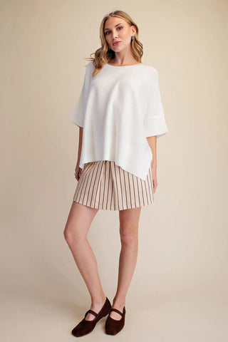 White oversized pullover sweater with short sleeves, ribbed hem, and relaxed boxy fit, styled with striped shorts.