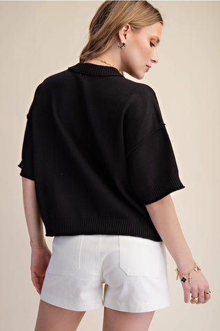 Black knit sweater with elbow-length sleeves, collar neckline, and seam detail, paired with white shorts.