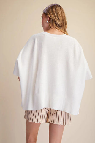 White oversized pullover sweater with short dolman sleeves, ribbed hem, worn over striped shorts.